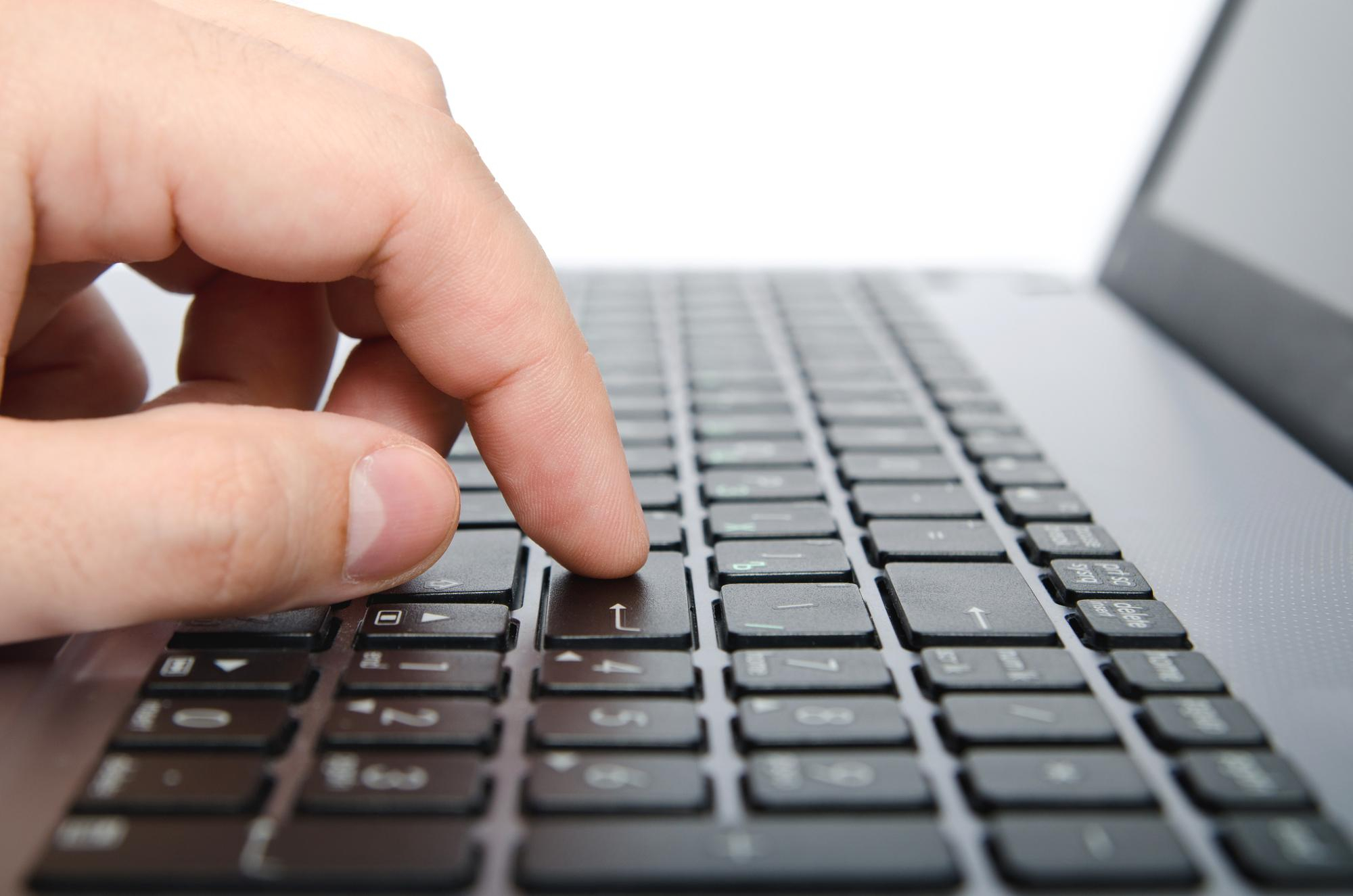 A hand pressing the enter key on a laptop keyboard.